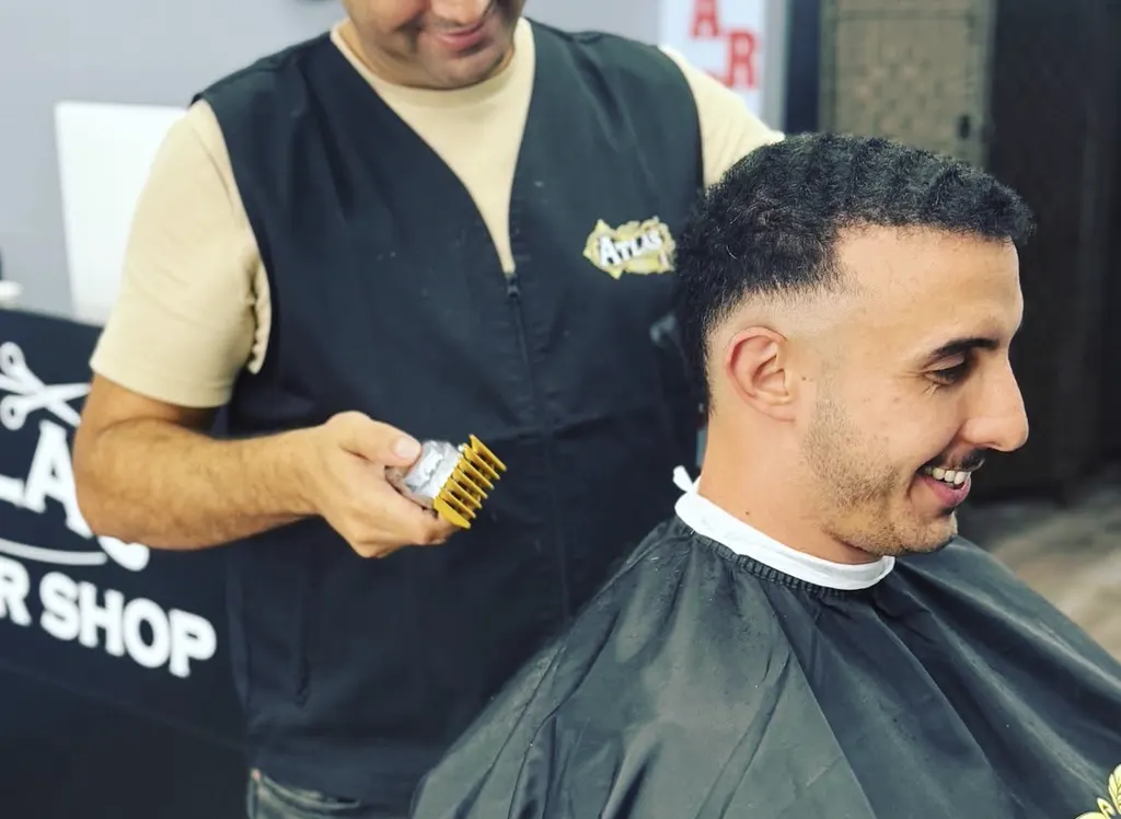 Barber at Atlas Barbershop using clippers to fade a client's haircut