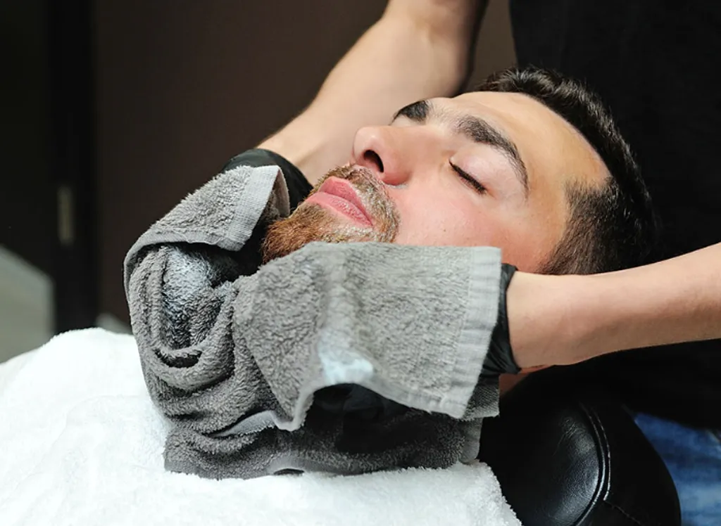 Barber at Atlas Barbershop applying a warm towel during a hot-towel shave