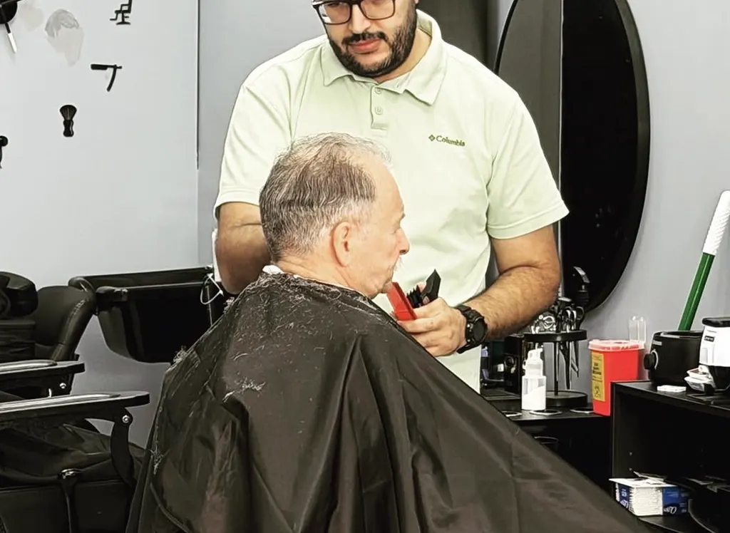 Barber carefully trimming an older client's beard and hairline at Atlas Barbershop