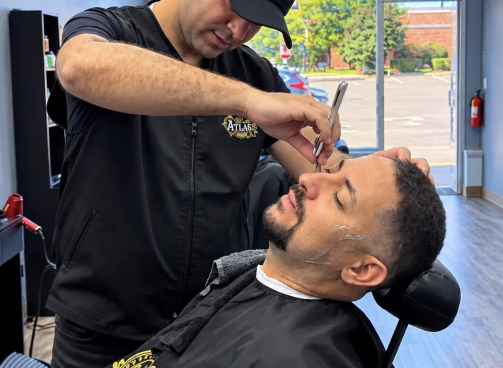Barber at Atlas Barbershop doing precise detail work near a client's temple